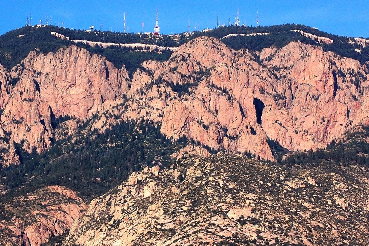 The granite face of the Sandia crest above Albuquerque catching low evening sun, the rock turned pink and the slope below it dropping away in boulders and scrub under a clear sky.