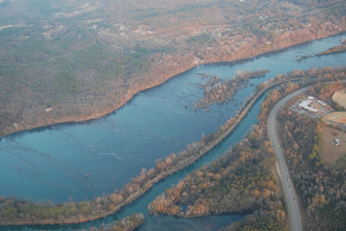 An aerial view of the Savannah River in winter, the broad shoaled main channel on the left, a narrower canal running parallel on the right, bare wooded banks between them and a highway along the edge.
