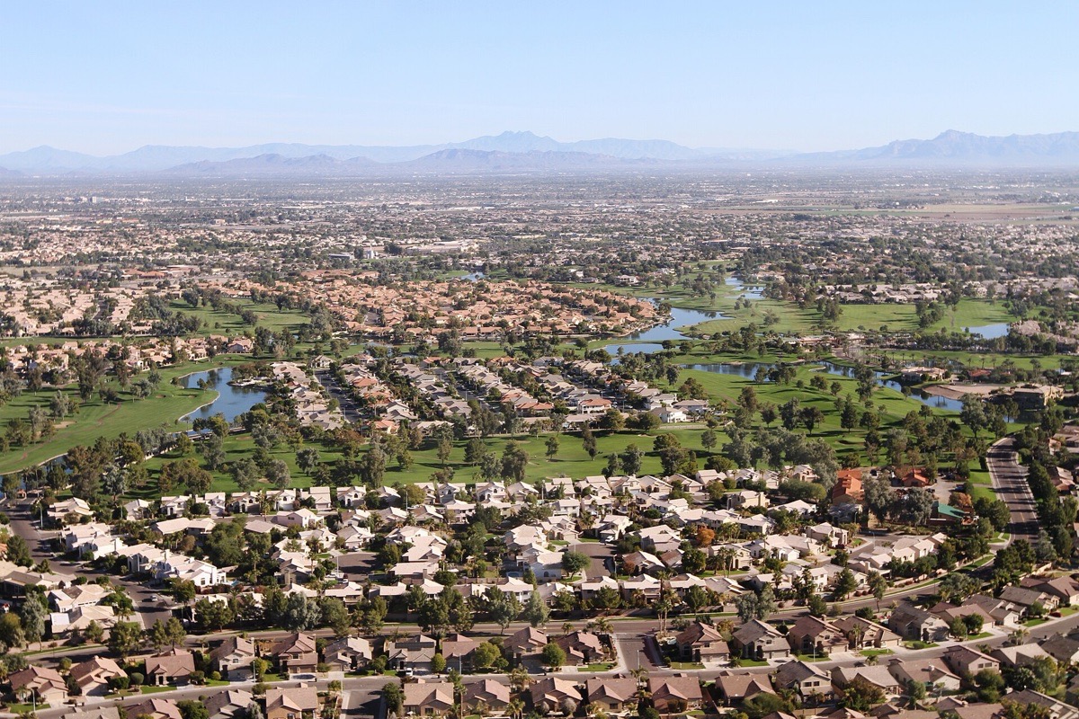 Chandler seen from the air, tile roofed houses and green fairways laid out in curves around narrow lakes, the pattern running flat to a distant line of desert mountains.