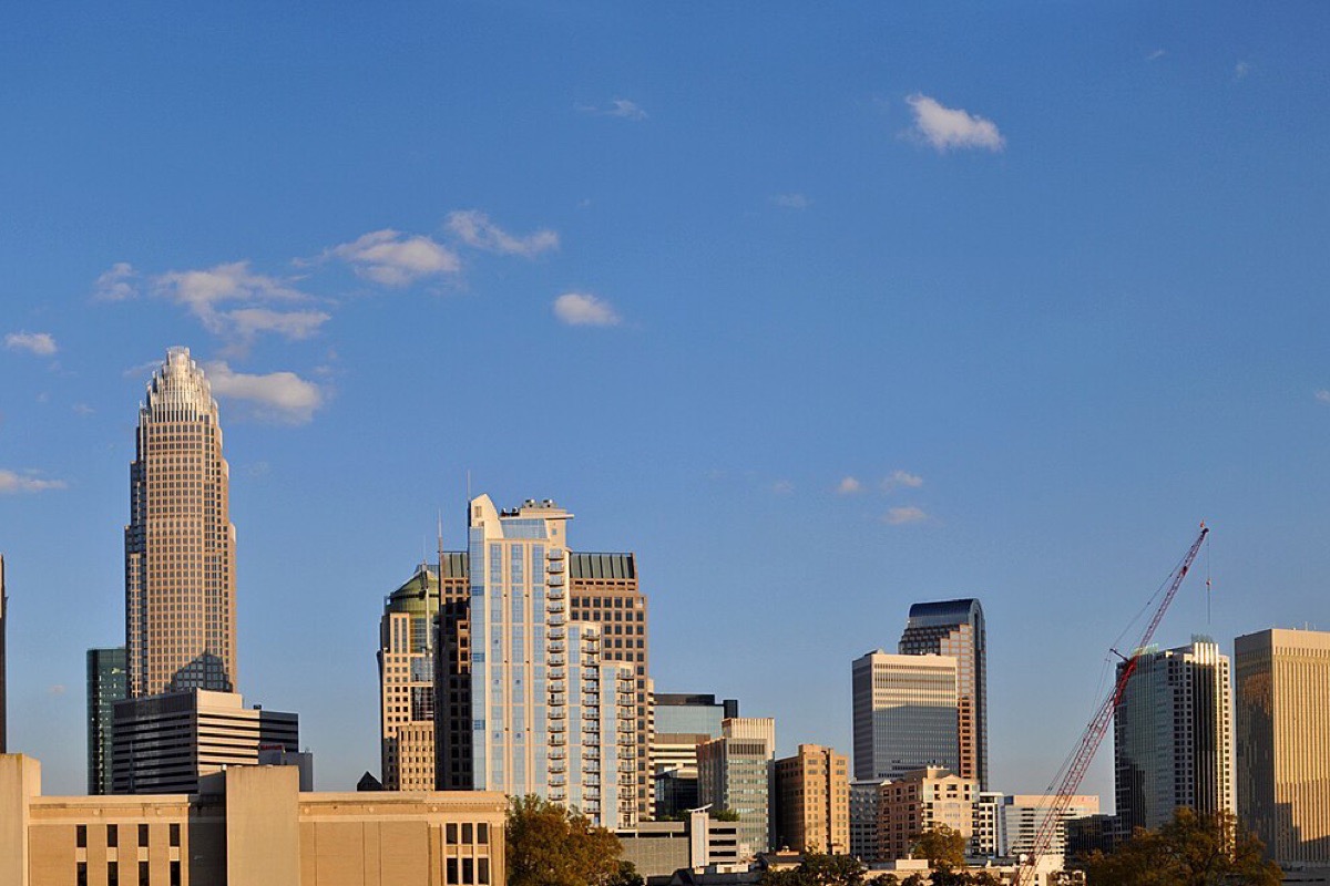 The Charlotte skyline under a blue sky with scattered cloud, the crowned tower standing above a close group of office blocks with a construction crane working on the right.