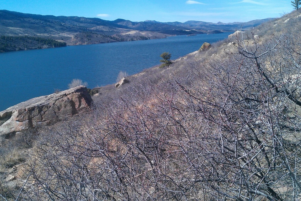 A deep blue reservoir held between dry rocky hogbacks west of Fort Collins, bare scrub and red sandstone in the foreground and the foothills running away under a clear sky.