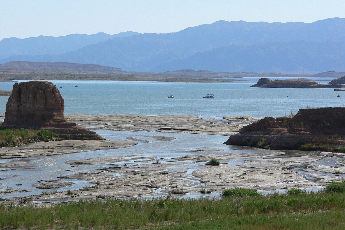 The shoreline of Lake Mead near Henderson at low water, pale exposed rock and mud in the foreground, a dark mesa standing out of the lake and desert mountains along the far side.