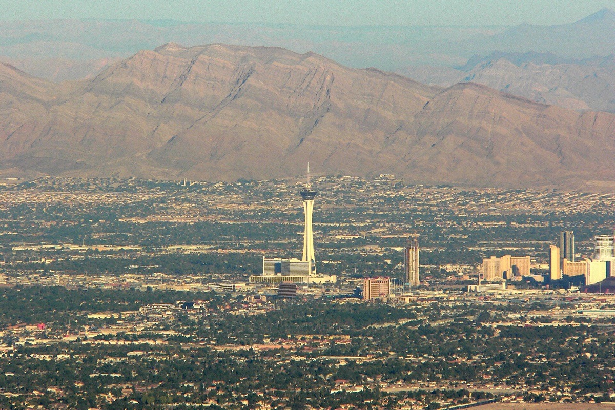 The Las Vegas valley seen from high ground, the tall observation tower and the cluster of resorts standing out of a flat grid of low buildings that runs to the foot of a long bare mountain range.