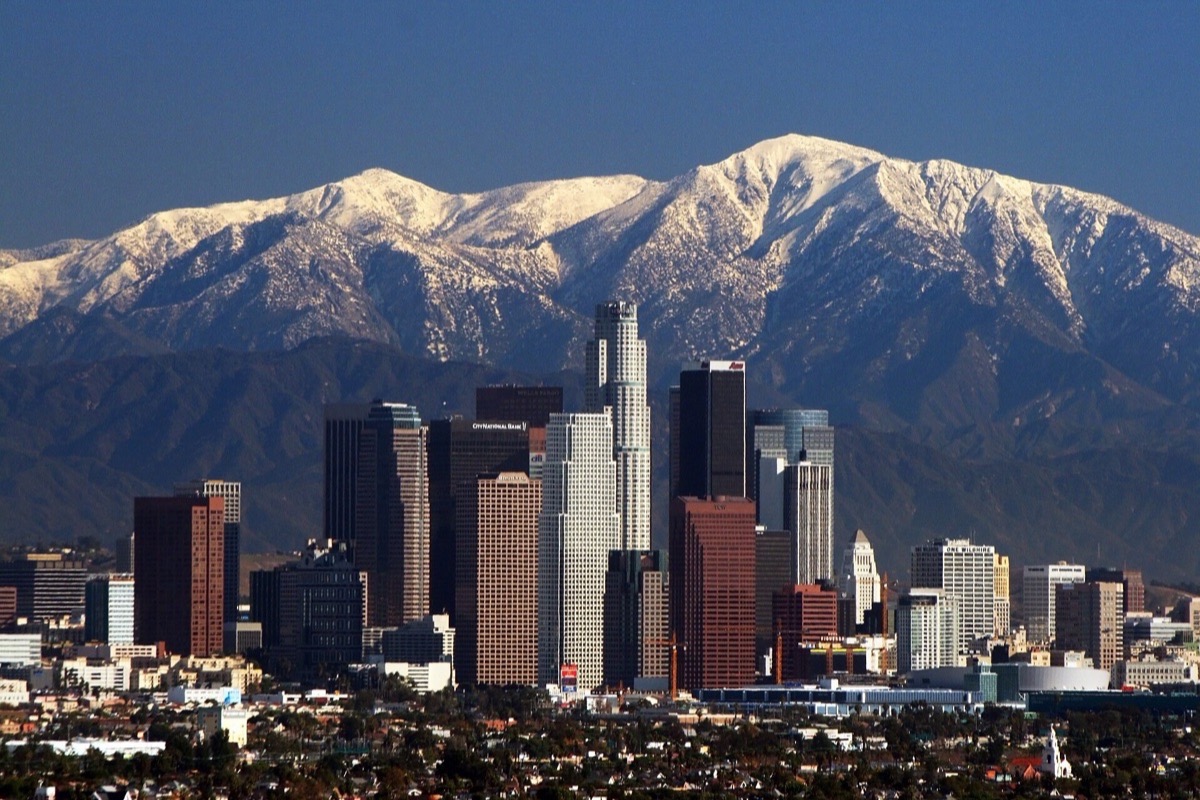 The Los Angeles skyline on a clear winter day with the snow covered San Gabriel mountains standing immediately behind it, the city running out flat below.