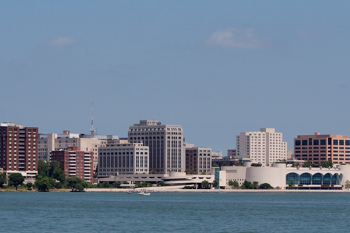 Madison seen from across Lake Monona, the capitol dome and the office blocks around it standing along the low shoreline under a clear sky, with flat blue water in front.