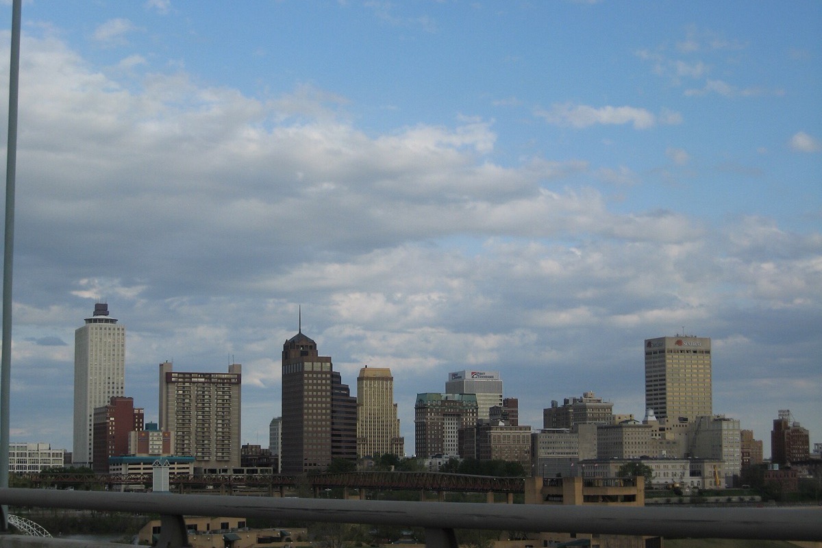 The Memphis skyline seen from the far side of the river under a tall bank of white cloud, a road bridge crossing low in front of the towers.