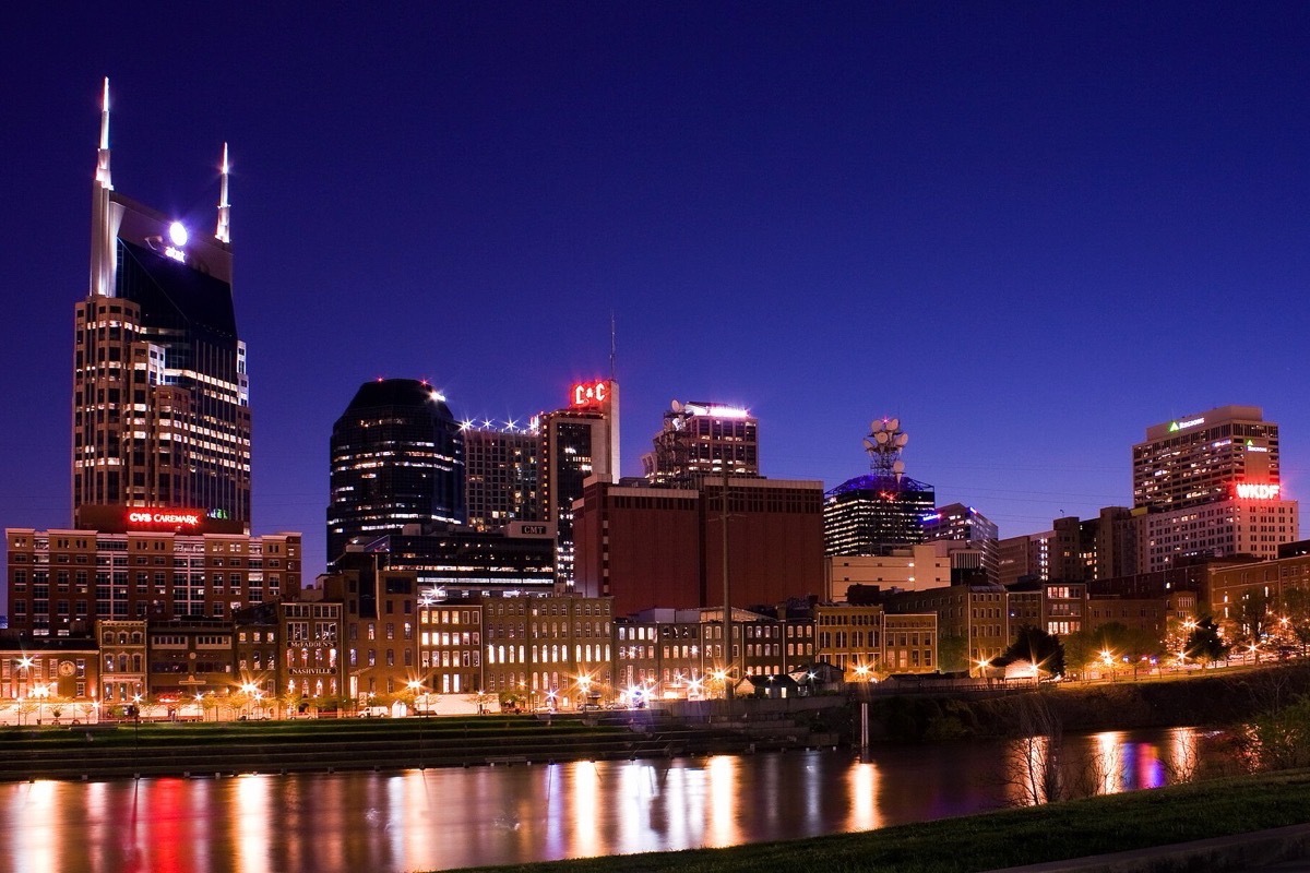 The Nashville skyline at night from across the Cumberland, the tall communications tower lit blue, the office blocks behind it and the whole line of lights drawn out in the water.
