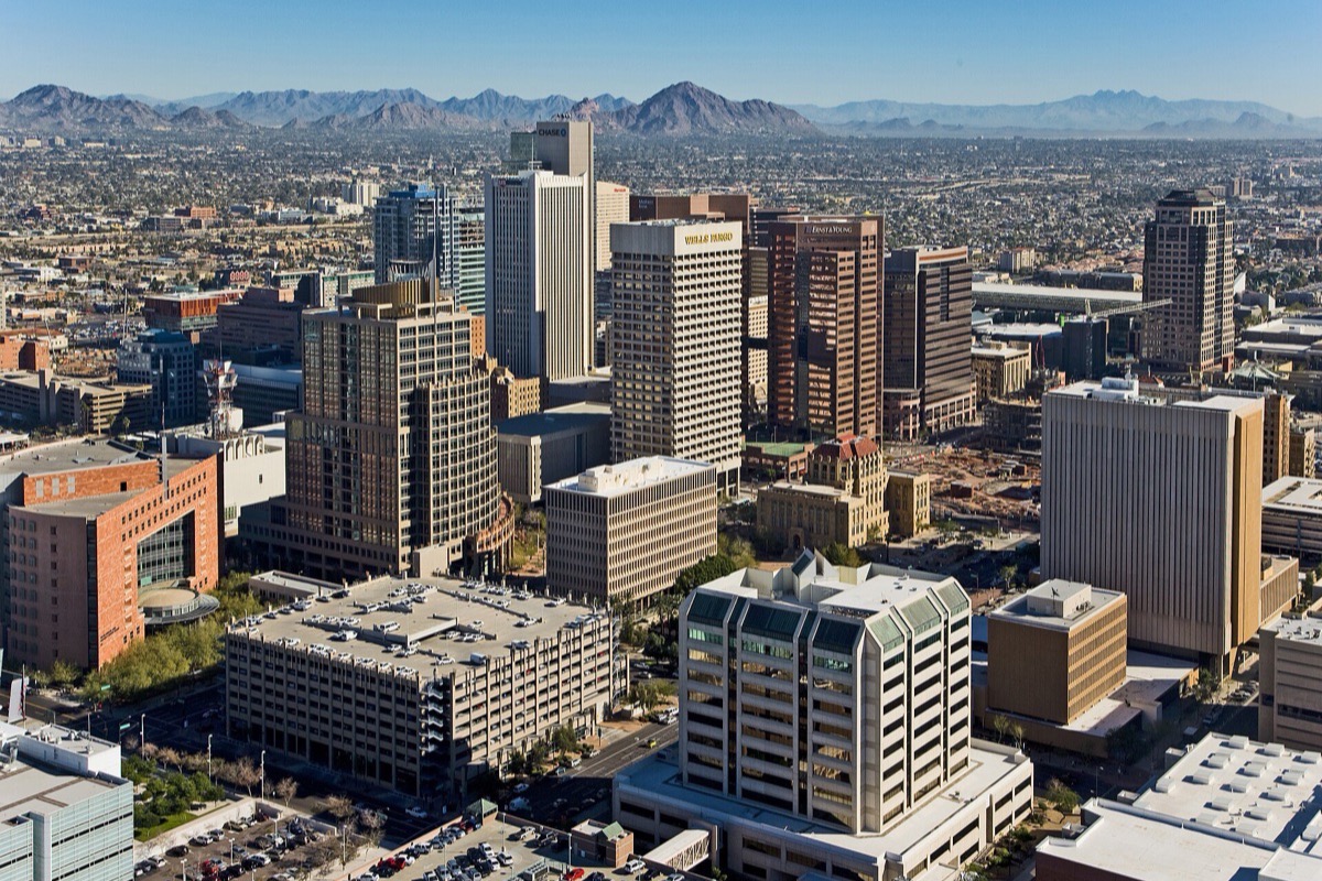 Phoenix seen from above looking out over the office towers and low blocks of the centre, the city running flat to the horizon with a long line of desert mountains beyond it.