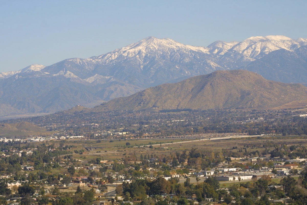 The Riverside valley seen from the hill above it, houses and trees running out flat to the horizon with the snow covered peaks of the San Bernardino range standing behind them.