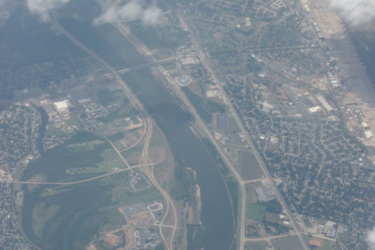 A high hazy aerial of the Red River between Shreveport and Bossier City, the channel curving between two built up banks with highways running alongside it.