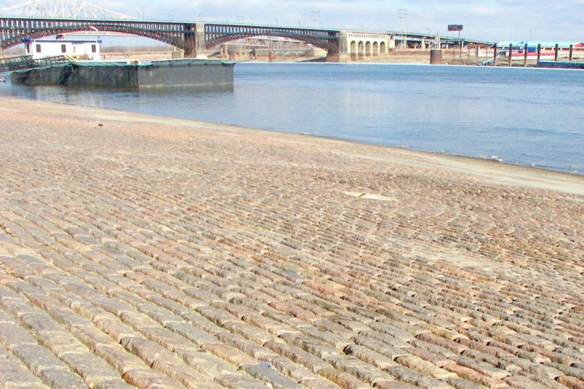 The old cobbled levee at St. Louis running down to the Mississippi in the foreground, with the steel spans of the Eads bridge crossing the river behind it.