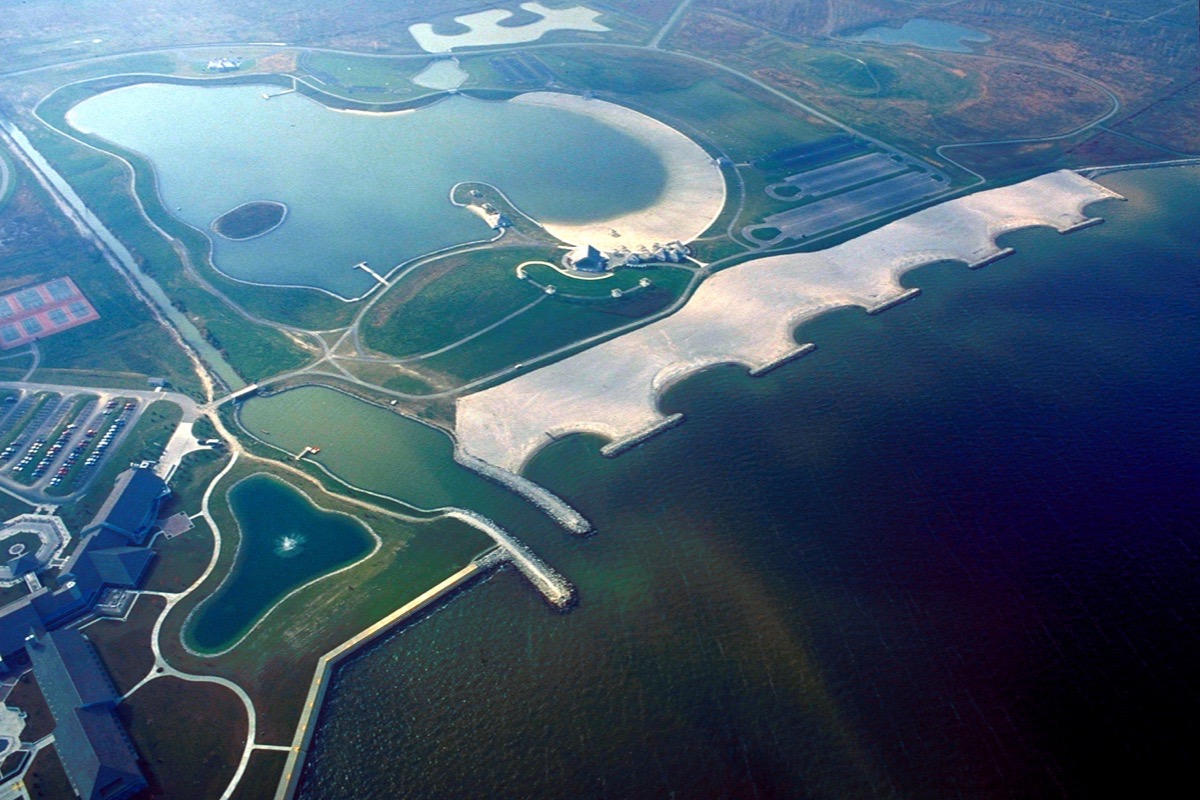 An aerial view of the Lake Erie shoreline near Toledo, engineered lagoons and a pale scalloped breakwater separating still inland water from the darker open lake.