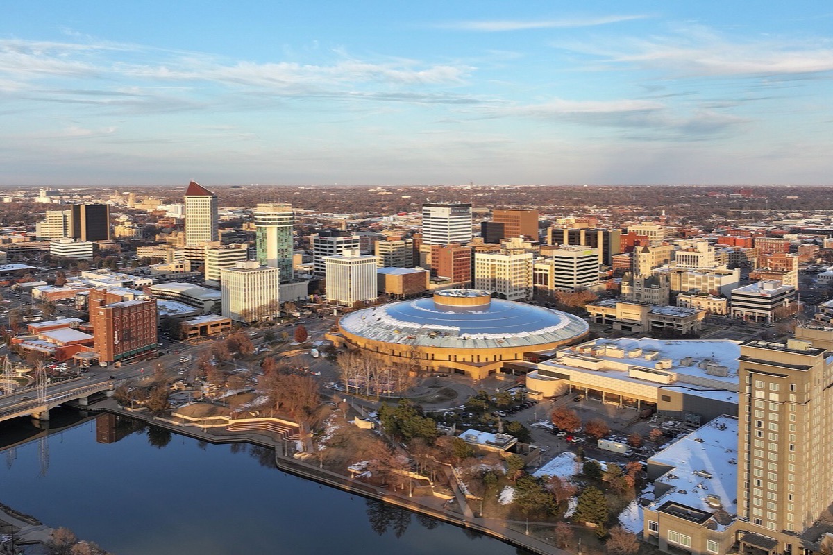 Wichita from above at the end of the day, the river curving through the middle of the city, a domed building beside it and low office blocks running out under a pale sky.