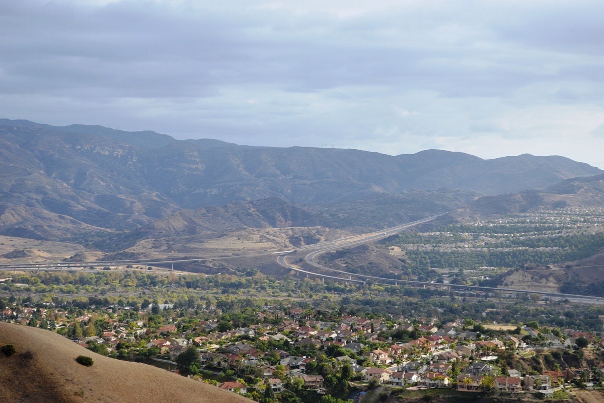 The Santa Ana Mountains standing behind the hills above Anaheim, a wide valley of houses and mature trees below them and a road curving up through the middle of it.