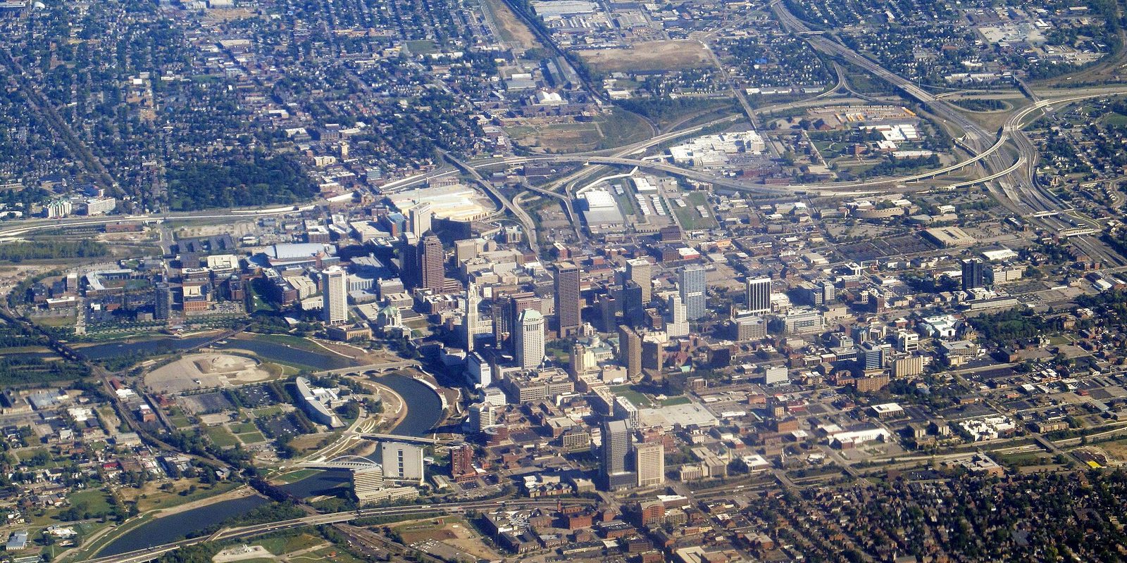 Aerial view of Columbus, with downtown towers beside a curving river and freeway interchanges and neighbourhoods spreading out to the horizon
