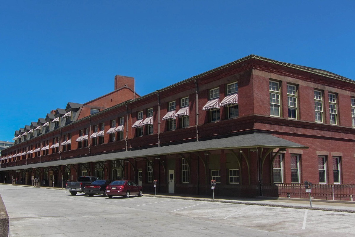 A long low red brick Pennsylvania station building with a run of arched windows and a canopy along the platform side, under a clear blue sky.