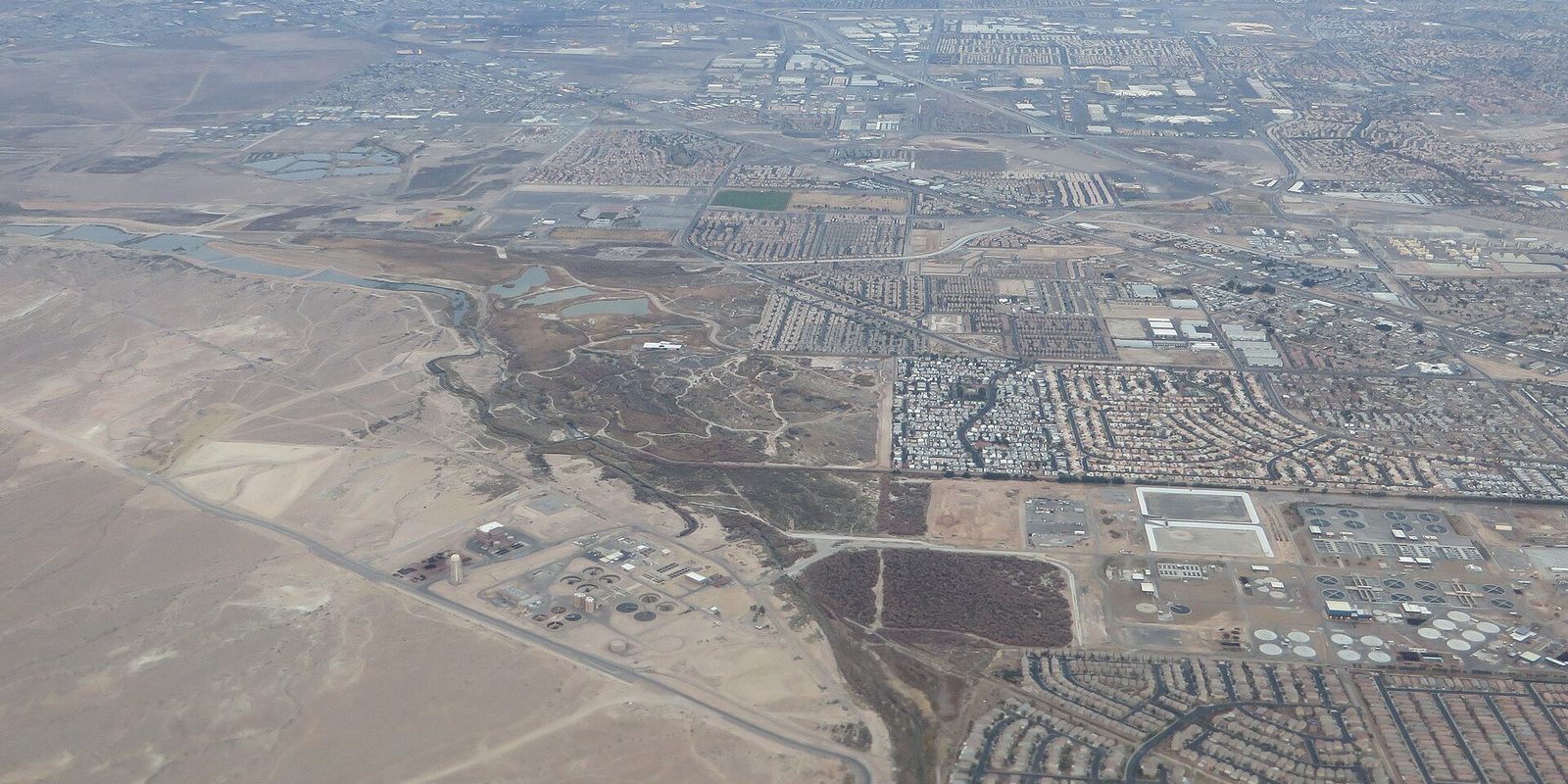 Aerial view over Henderson, Nevada, where curving housing tracts and industrial lots meet bare tan desert and a hazy valley horizon