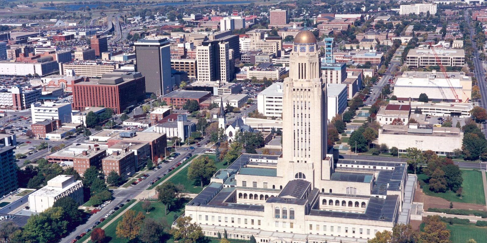 Aerial view over downtown Lincoln, Nebraska, with the State Capitol's gold-domed tower rising above low office blocks and tree-lined streets