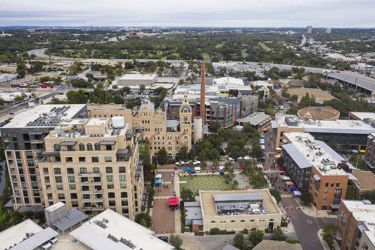 San Antonio, Texas: an aerial over the Pearl District, the historic brewery and its brick smokestack above a plaza of market tents, under an overcast sky.