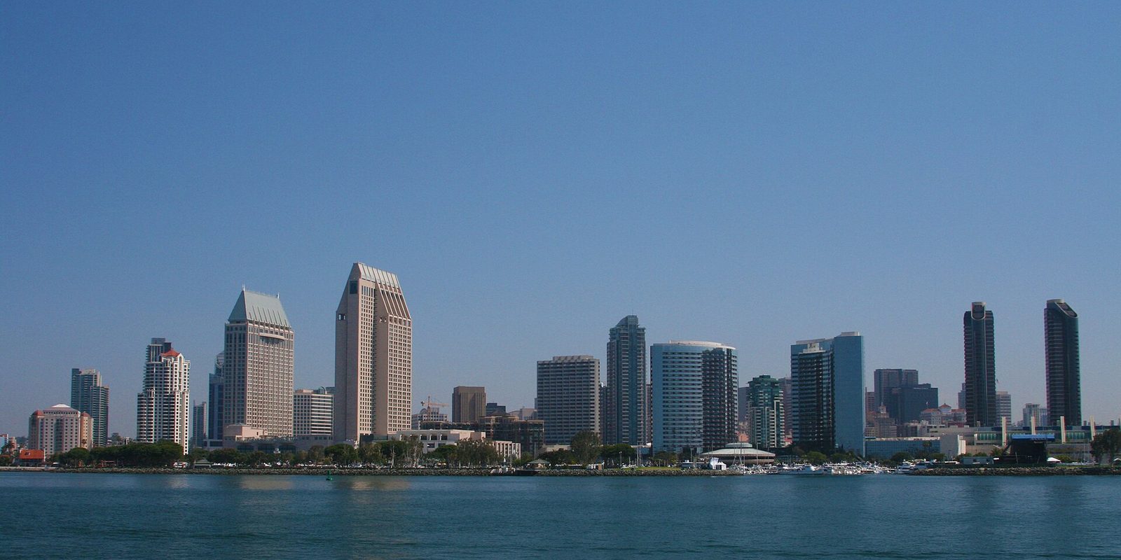 San Diego's downtown towers rising above the bay, boats moored along the waterfront under a clear blue sky