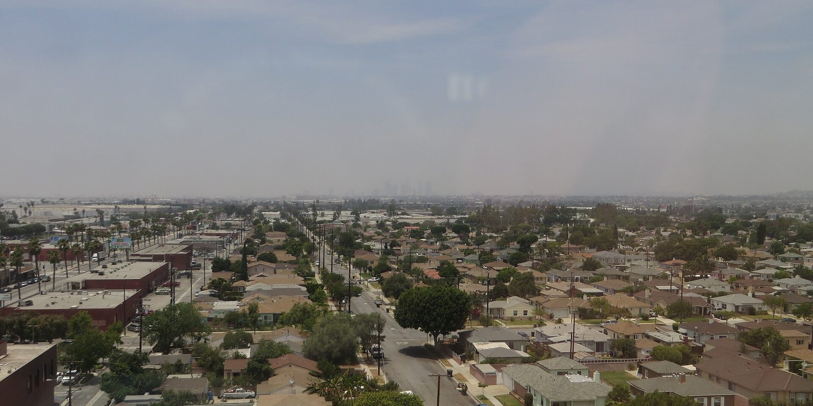 Santa Ana rooftops and palm-lined streets spreading flat toward a hazy cluster of distant towers