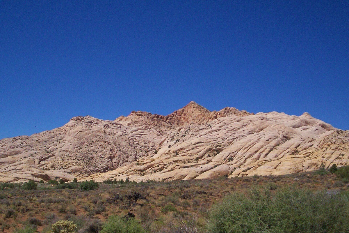 A long ridge of swirled white and red Utah sandstone rising above green desert scrub under a deep blue sky.