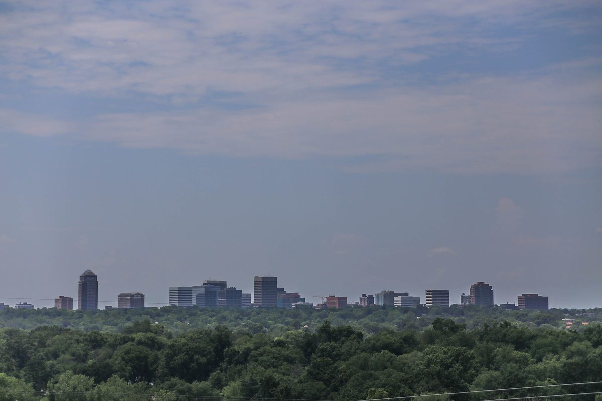 St. Louis, Missouri: a hazy cluster of mid-rise office towers on the horizon above a dense band of green treetops.