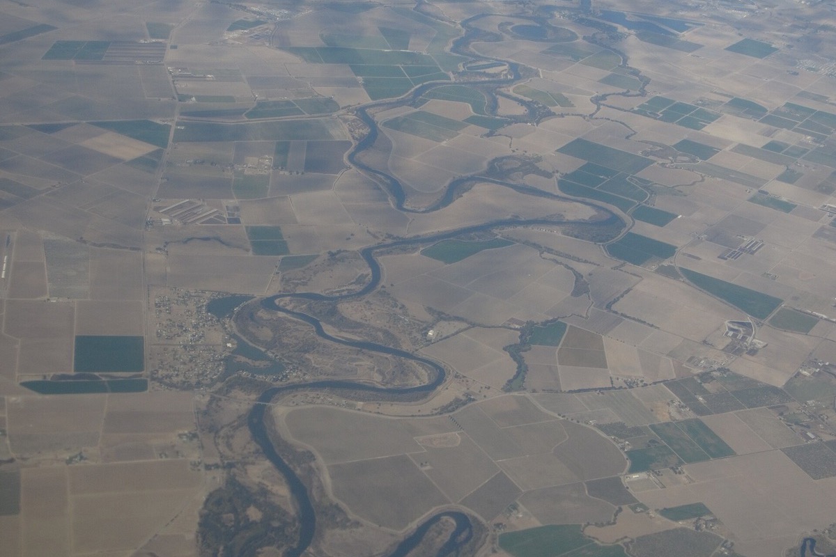 The San Joaquin delta from the air, a river winding in tight loops through a flat grid of green and pale fields that runs away to the horizon in haze.