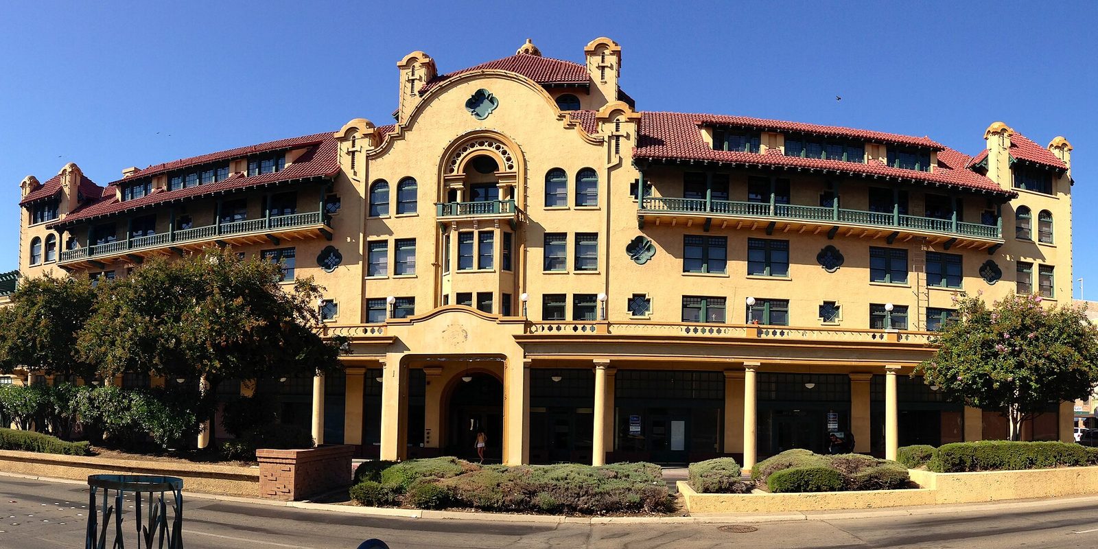 A landmark Spanish Revival building in downtown Stockton, tan stucco with a red tile roof and arched windows, under a clear deep-blue sky