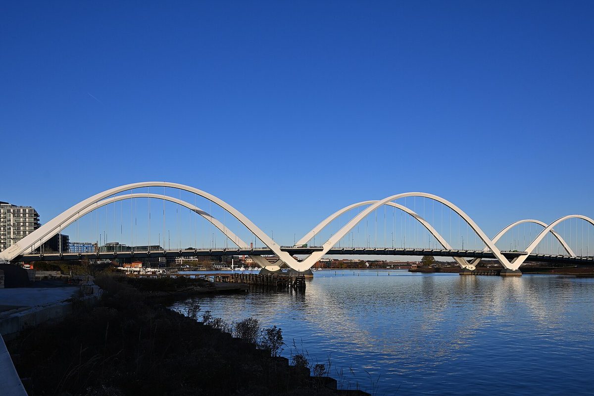 Washington's white arched Frederick Douglass Memorial Bridge spanning the calm Anacostia River under a deep blue cloudless sky.