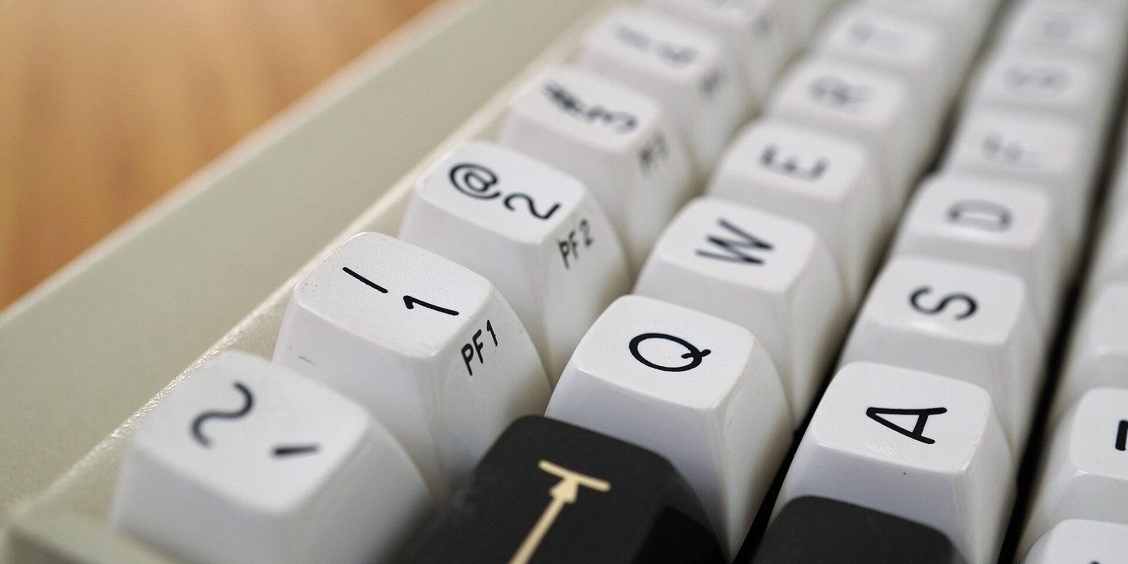 White keycaps on a vintage beige computer keyboard, lettered Q, W, A and S with numerals and small PF1 and PF2 function labels.