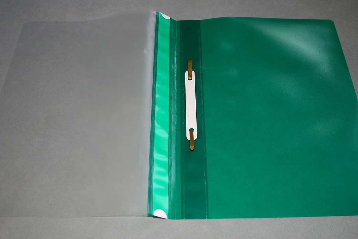 An open green plastic report folder with a clear front cover and a gold metal prong fastener, lying on a grey surface.