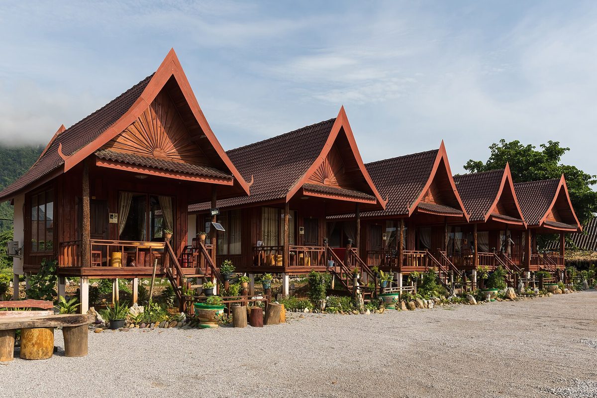 A row of identical wooden bungalows with steep red tiled gables, raised on stilts beside a gravel lot.