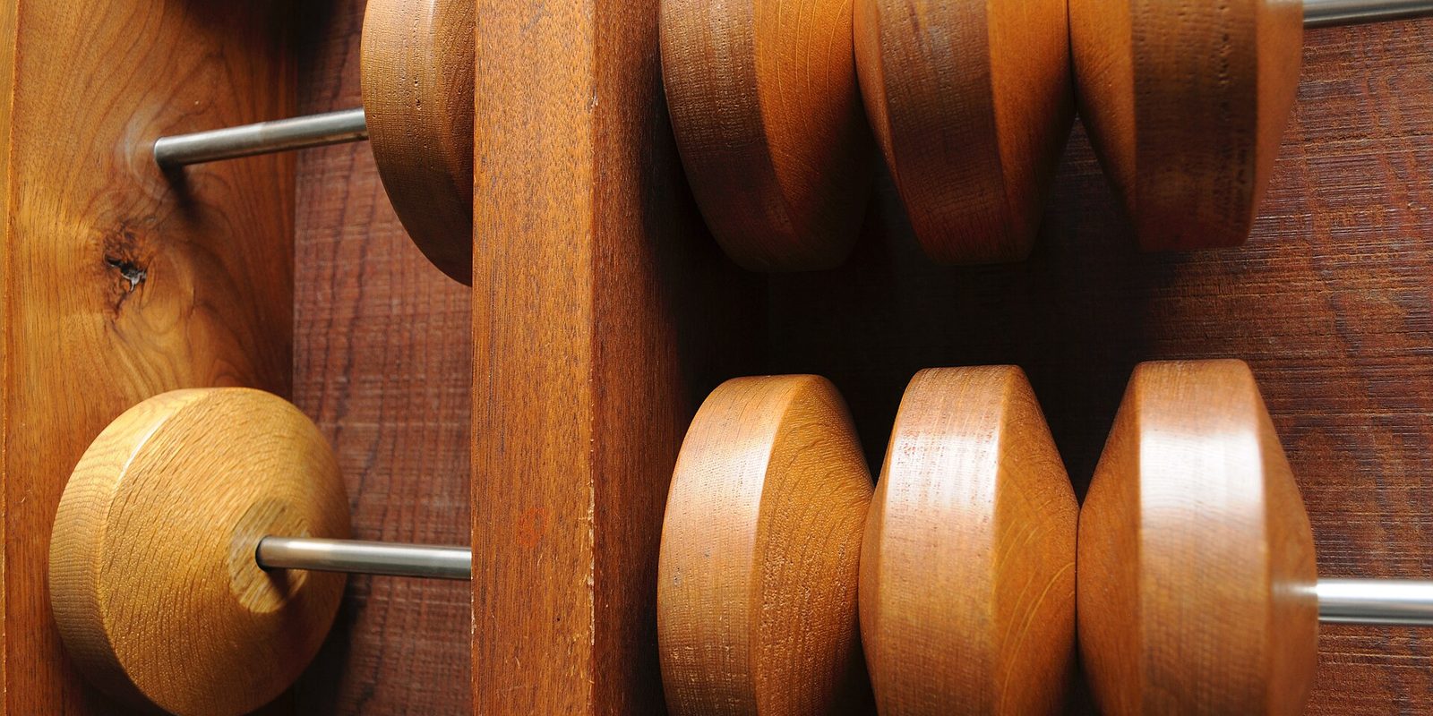 Rounded wooden abacus beads strung on thin steel rods in a dark hardwood frame, lit warmly from one side.
