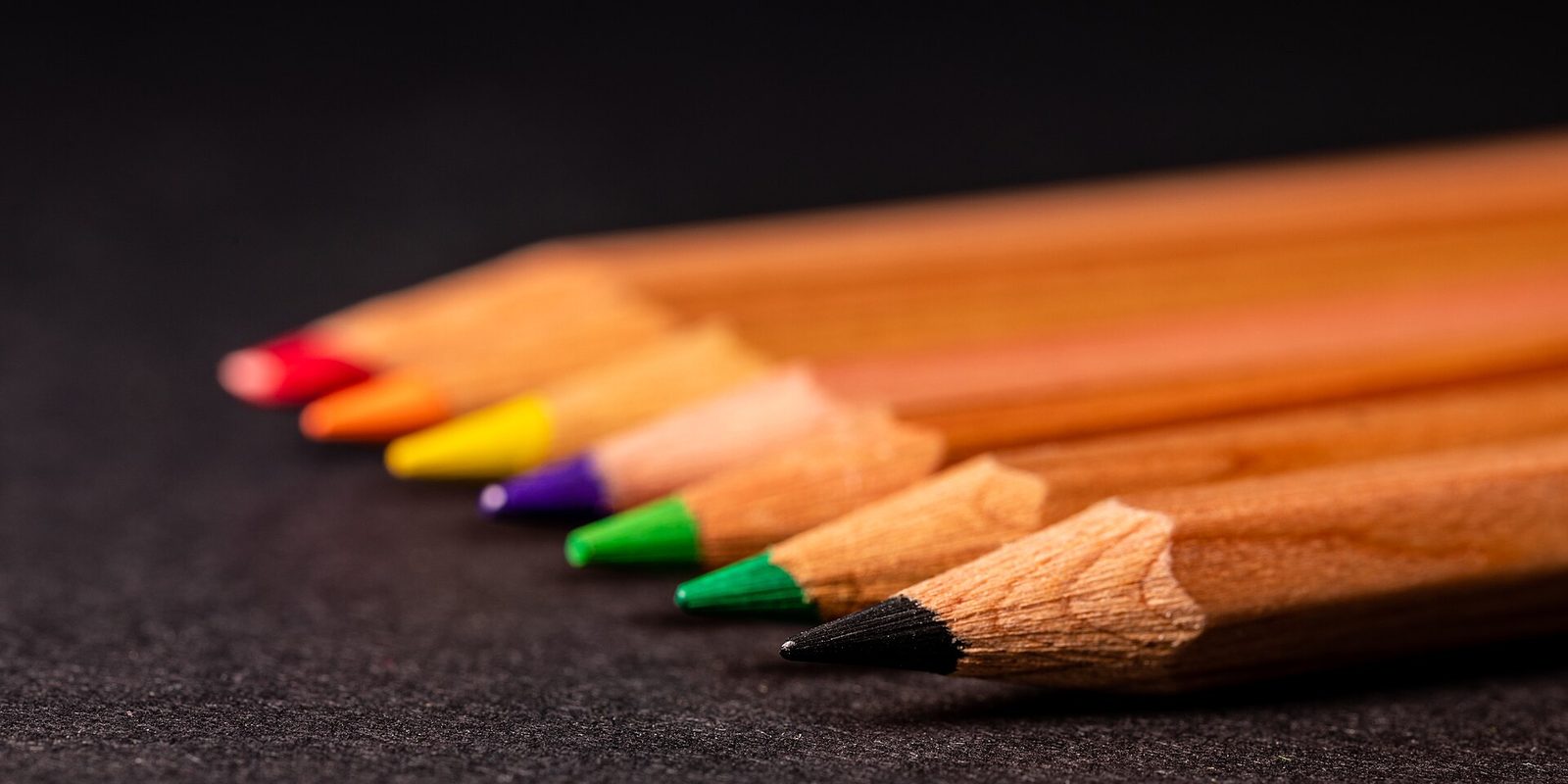 Close-up row of sharpened coloured pencils and a black graphite pencil on a dark surface