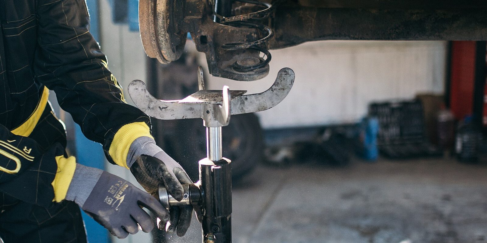 Gloved hands positioning a jack stand under the raised suspension of a vehicle in a garage