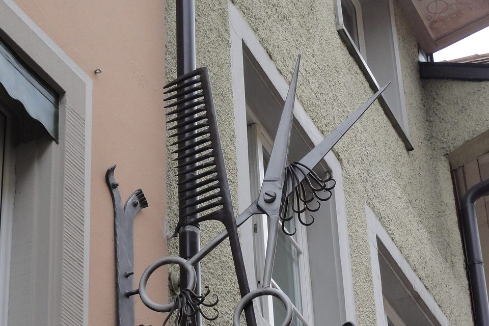 A wrought iron shop sign shaped like oversized scissors and a comb mounted on a building wall