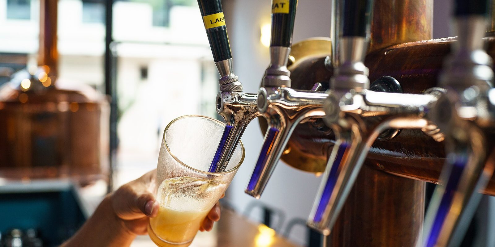 A glass held under a row of chrome and copper taps as lager pours into it