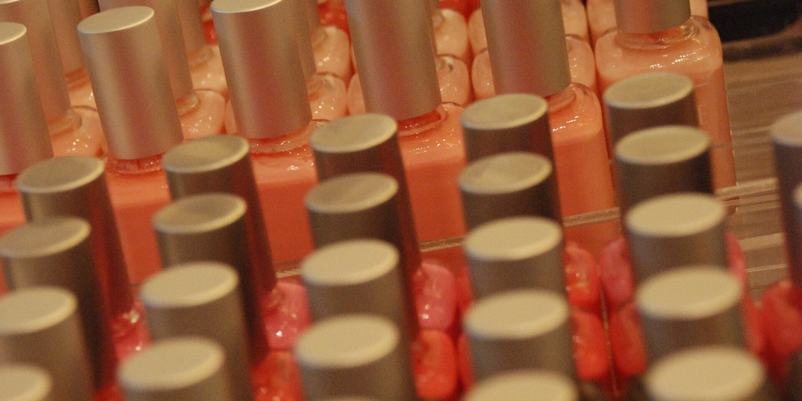 Close up rows of coral and pink nail polish bottles with matching metallic caps
