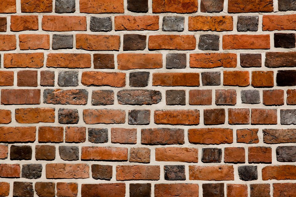 Close view of a weathered brick wall in mixed red, orange and dark grey brick
