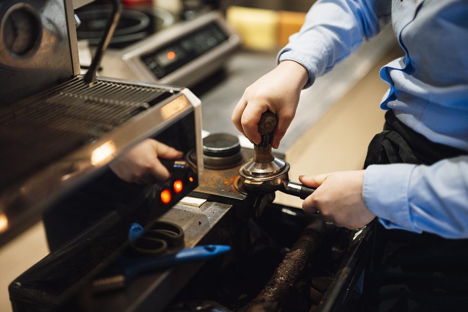 Hands tamping ground coffee into a portafilter beside an espresso machine