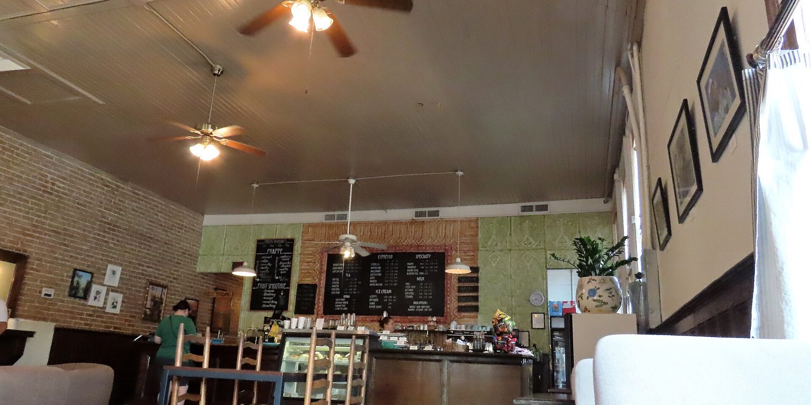 Interior of a coffee shop with chalkboard menus, exposed brick, ceiling fans and a bakery counter