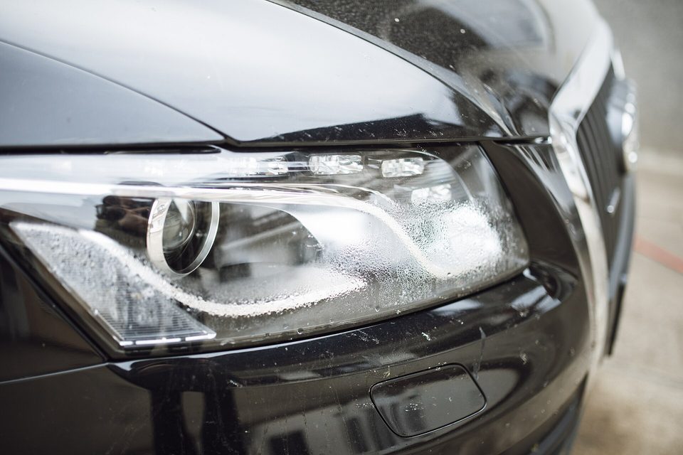 Close-up of the headlight and front corner of a black car beaded with water droplets