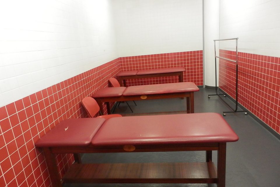 An empty treatment room with two padded exam tables against red tiled walls