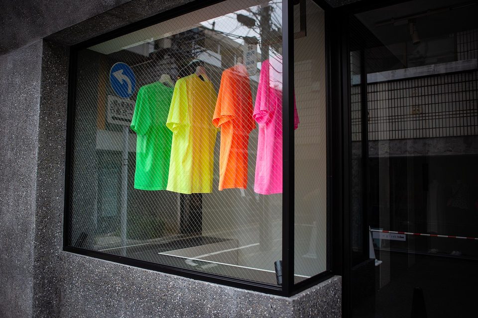 Four neon green, yellow, orange and pink T-shirts hanging in a shop window