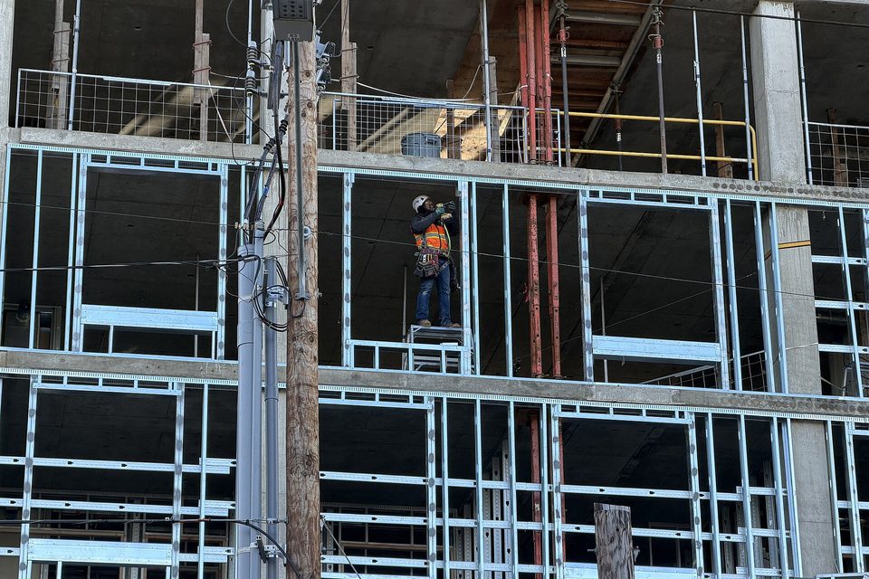 A worker in a hard hat and safety vest standing on a platform among metal stud framing on a concrete building