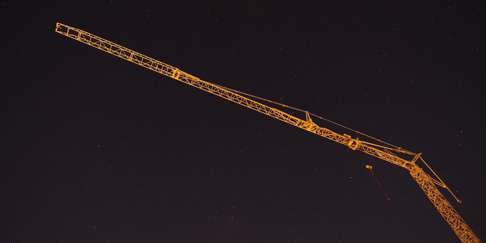 A yellow lattice tower crane jib lit against a dark night sky full of stars