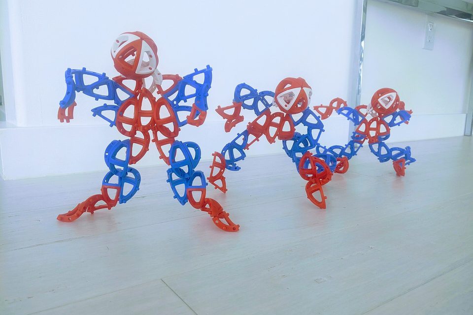 Three figures built from interlocking red and blue plastic construction pieces standing on a pale floor