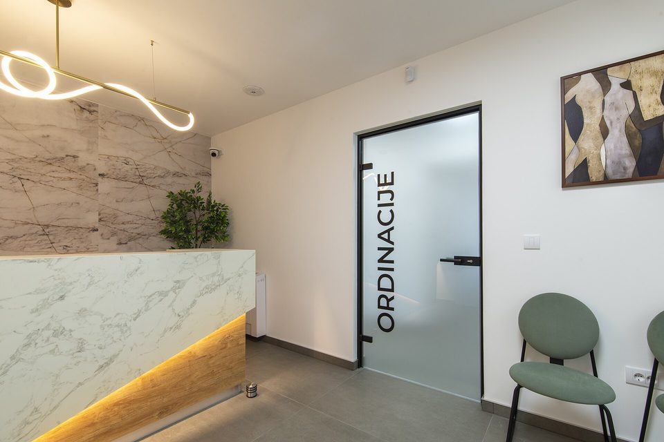 A small clinic reception area with a marble front desk, a frosted glass door and a green waiting chair