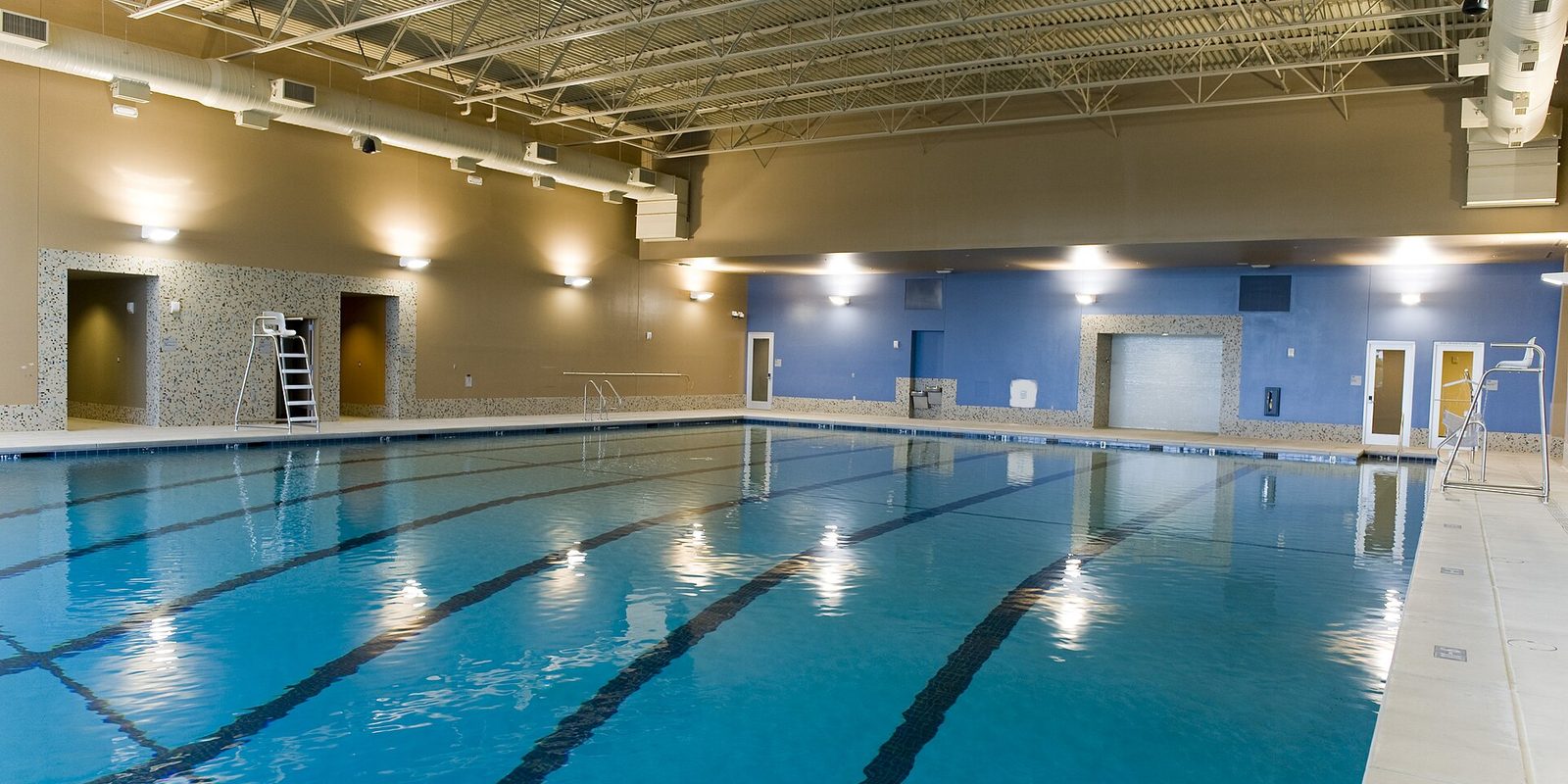 An empty indoor lap pool with lane lines, a lifeguard chair and blue and tan walls